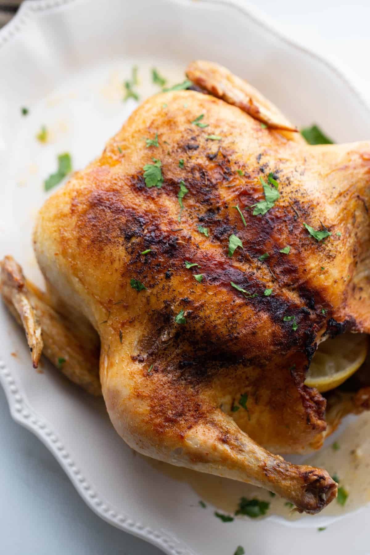 An air fryer roasted whole chicken on a pretty white platter.