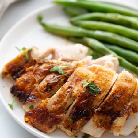 Sliced chicken air fryer chicken breast on a white plate with green beans on the side.