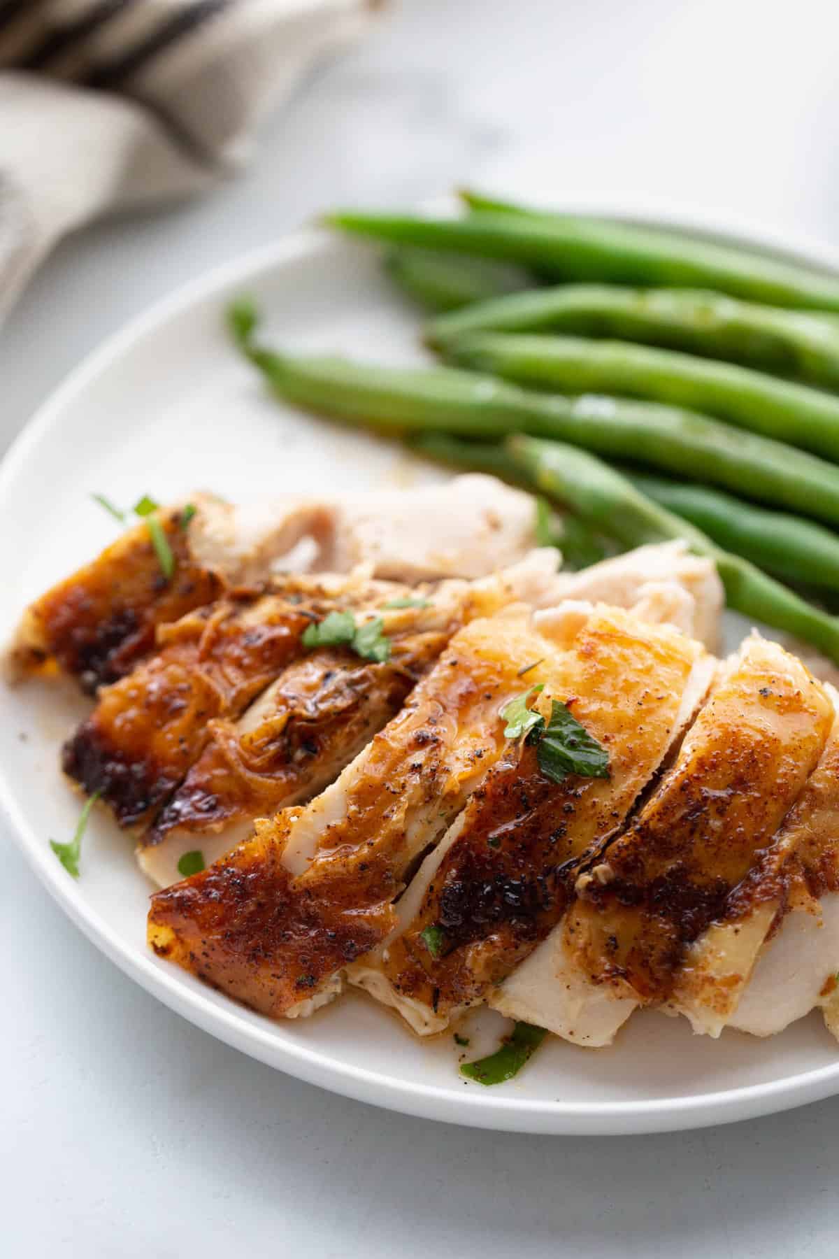 Sliced chicken air fryer chicken breast on a white plate with green beans on the side.