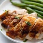 Sliced air fryer whole chicken on a white plate with a side of green beans.