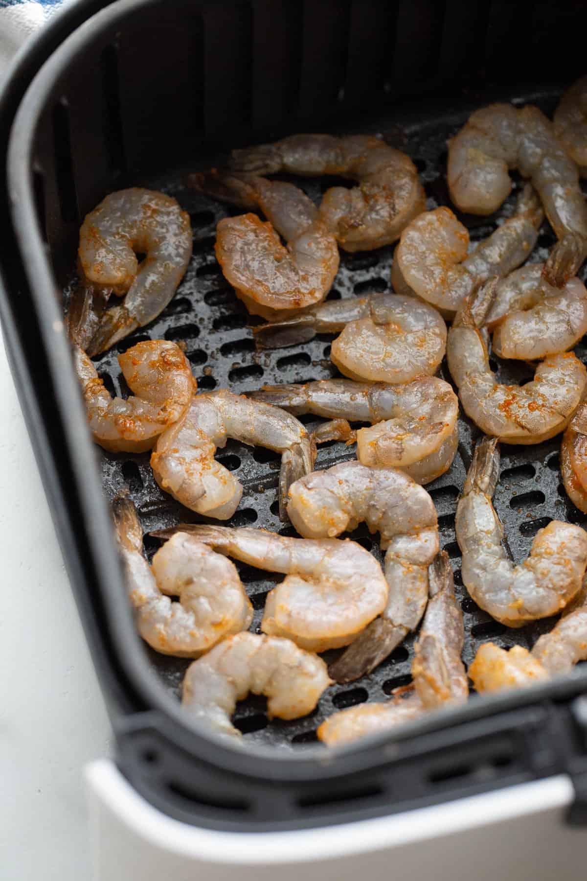 Raw shrimp in an air fryer basket.