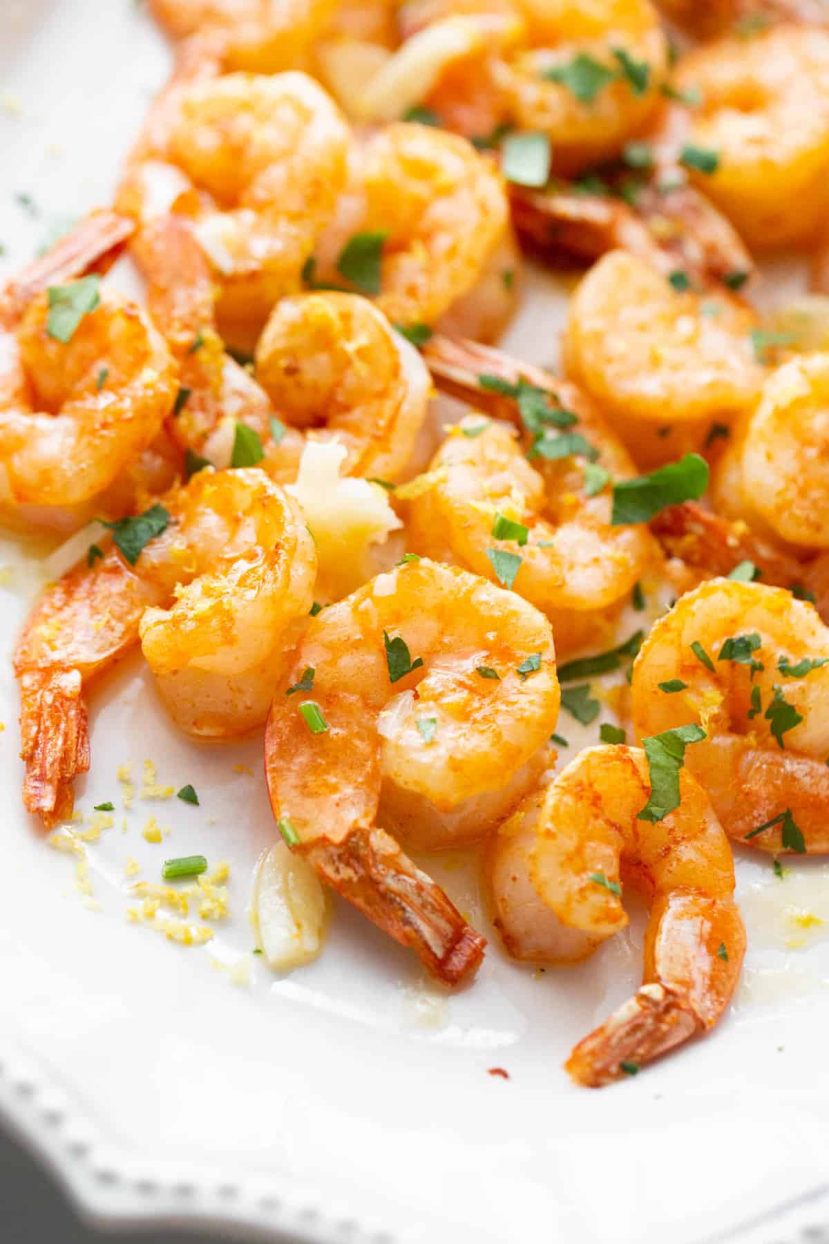 Close up of Air Fryer Shrimp on a white platter drizzled with garlic butter sauce.