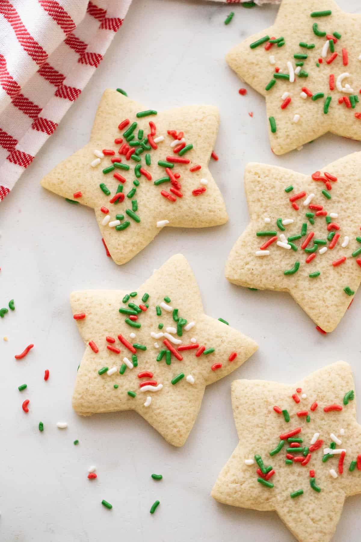 Star shaped dairy free sugar cookies on a white counter near a red and white striped kitchen towel.