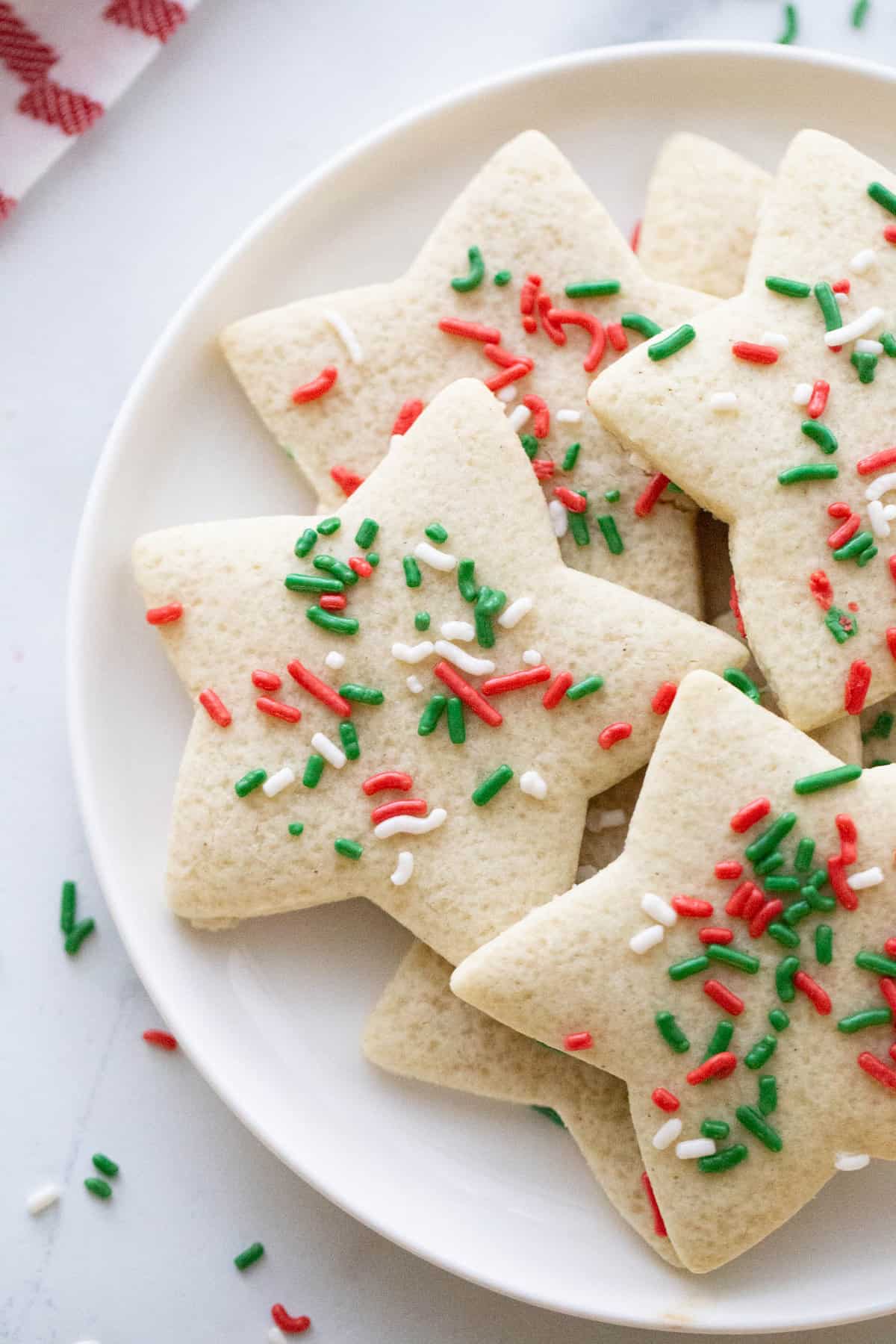 A white round plate with a stack of gluten free star shaped sugar cookies with Christmas colored sprinkles.