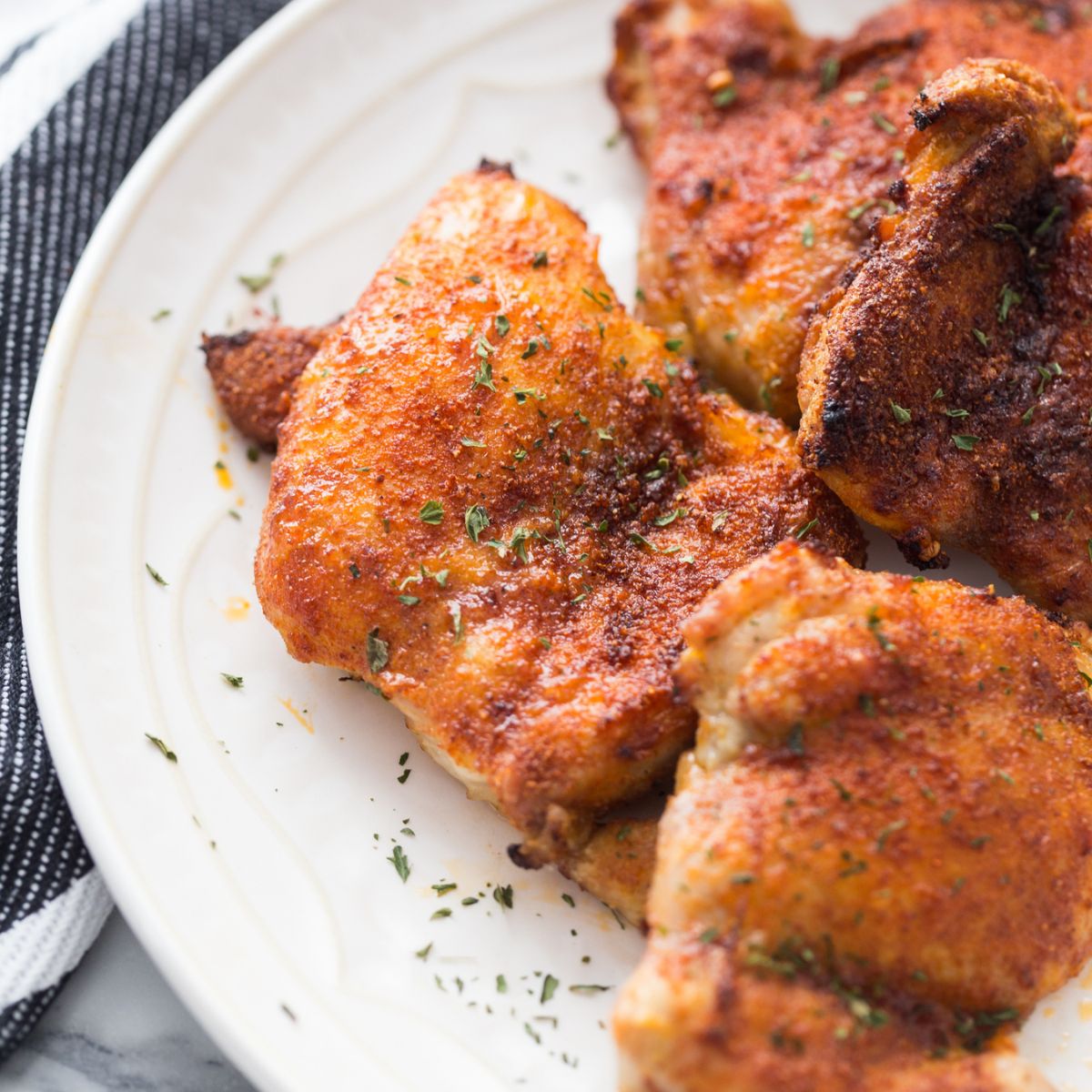 A plate of Boneless Skinless Air Fryer Chicken Thighs with fresh and dried herbs and spices.
