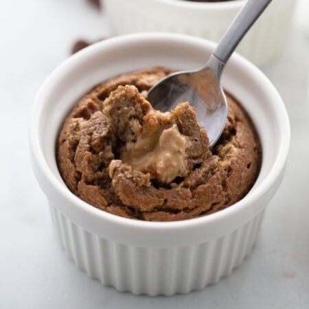 Baked oatmeal in a white ramekin with someone spooning out a bite with melty peanut butter baked inside.