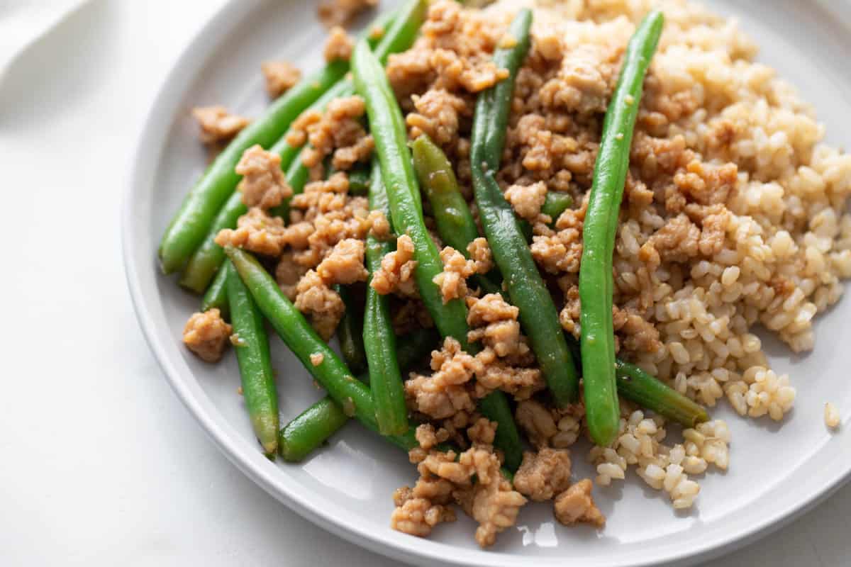 A close up plate of ground chicken stir fry with green beans over brown rice.