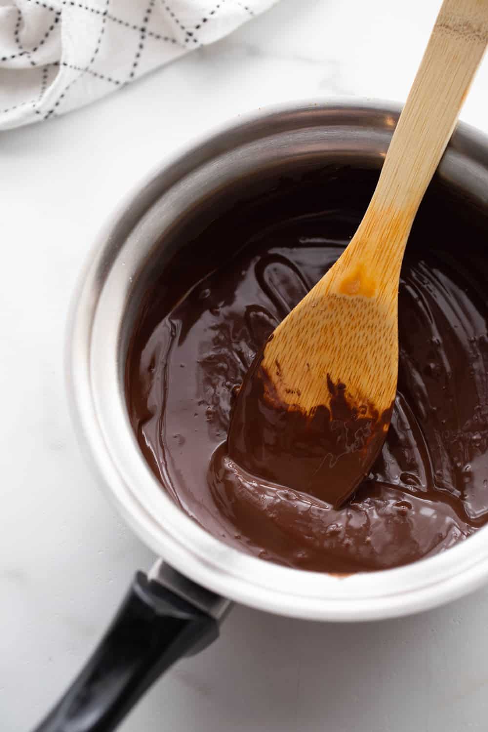 Wooden spoon in a small pot of melted chocolate.