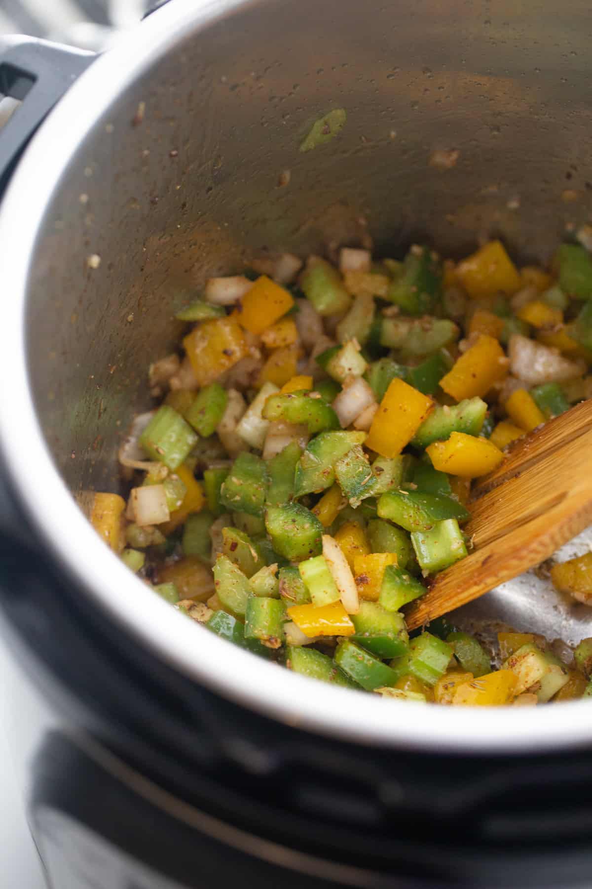Green and yellow bell peppers being sauteed along with onion in an Instant Pot preparing jambalaya.