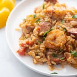 A white plate with brown rice, shrimp, peppers, and chicken sausage.