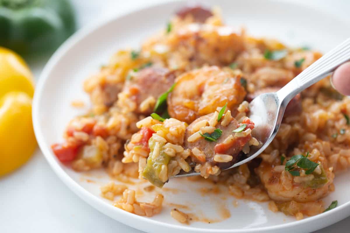 A fork full of instant pot jambalaya with yellow and green pepper sitting close by.