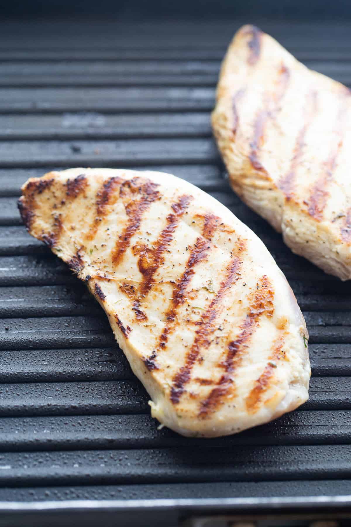Two Grilled chicken breasts with grill marks on a grill pan.