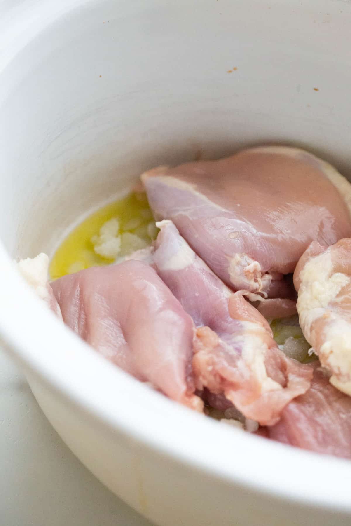 Chicken thighs, onions, and olive oil in a crock pot.