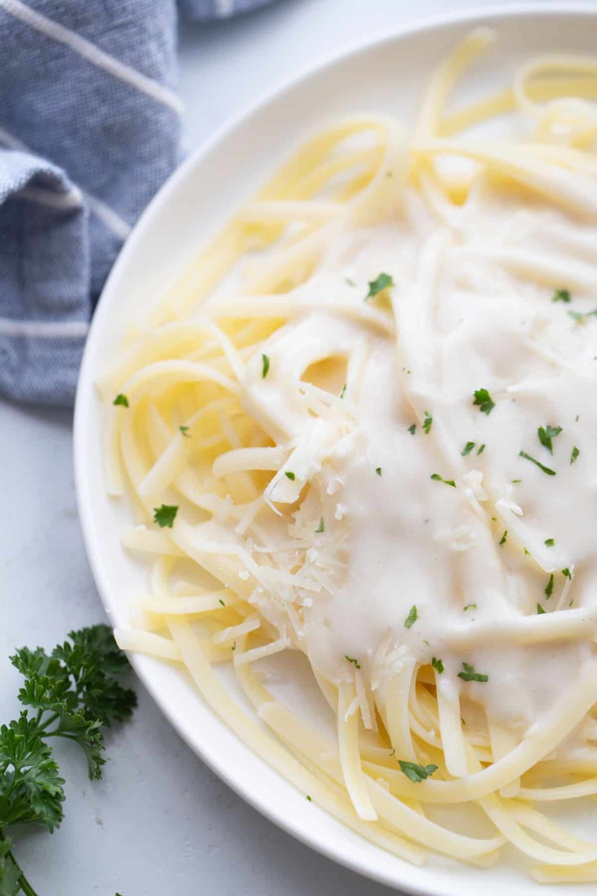 A plate of healthier fettuccini alfredo garnished with fresh parsley.