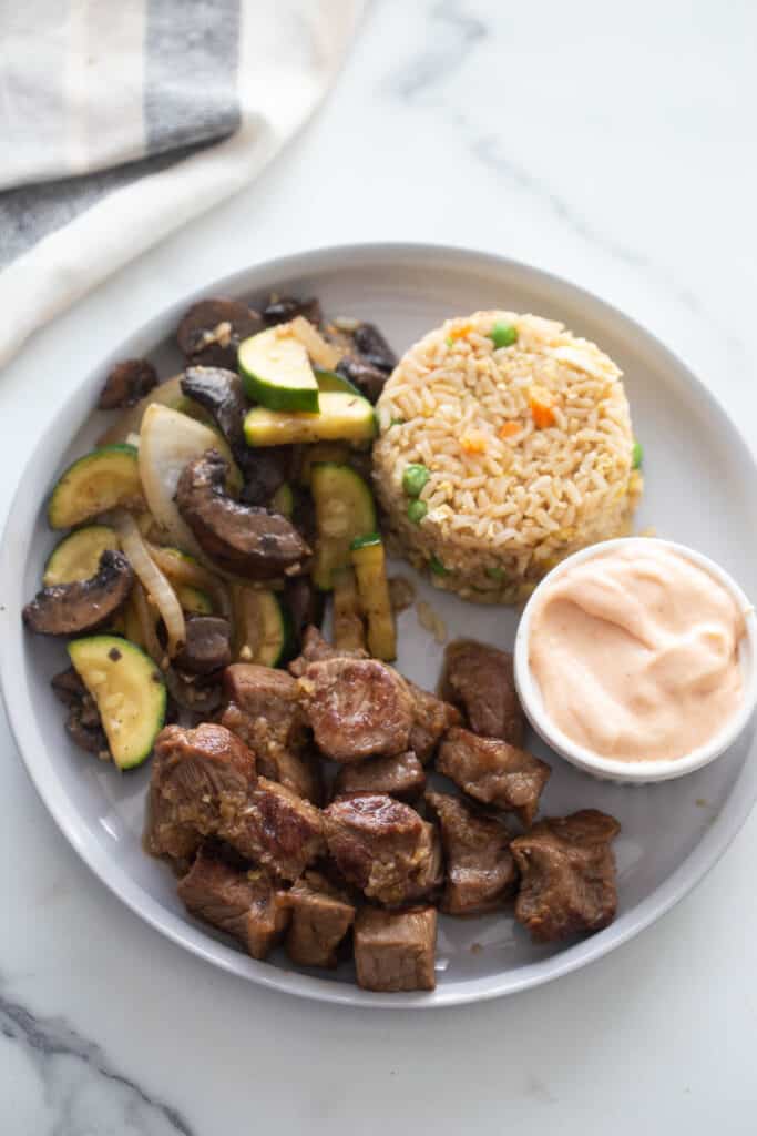 Cubed hibachi steak drizzled with ginger sauce, stir fried veggies, vegetable fried rice, and a ramekin of yum yum sauce.
