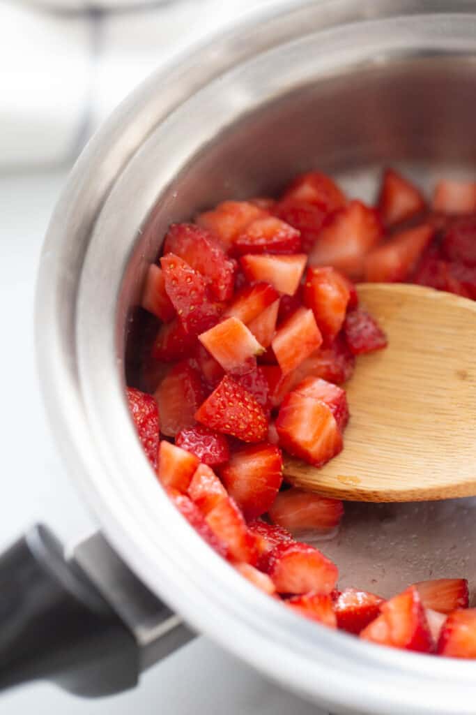 Diced strawberries in a pot with a wooden spoon.
