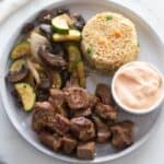 White plate with hibachi steak, hibachi veggies, yum yum sauce, and fried rice.