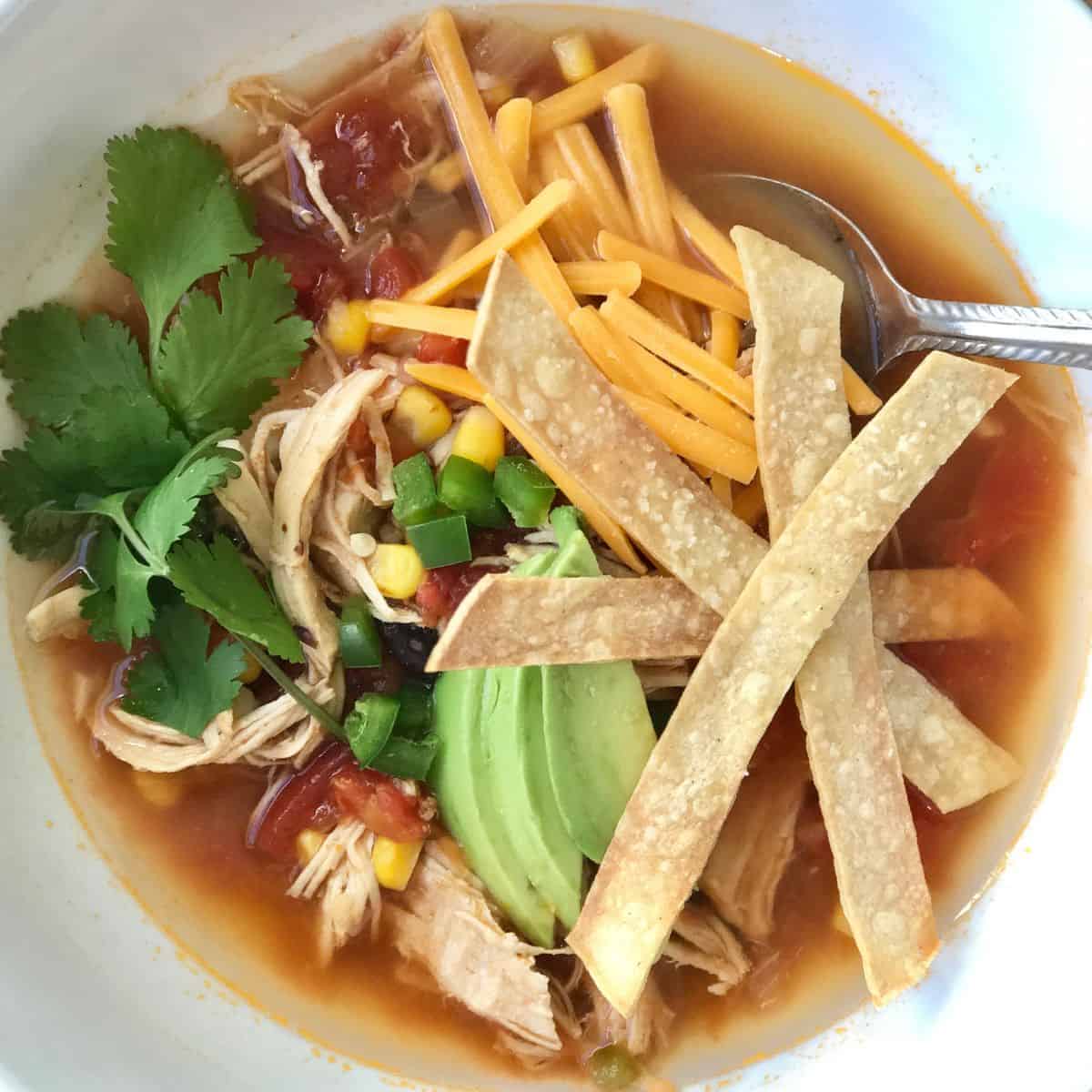 Bowl of Chicken Tortilla soup topped with jalapeno, cheddar cheese, and tortilla strips.