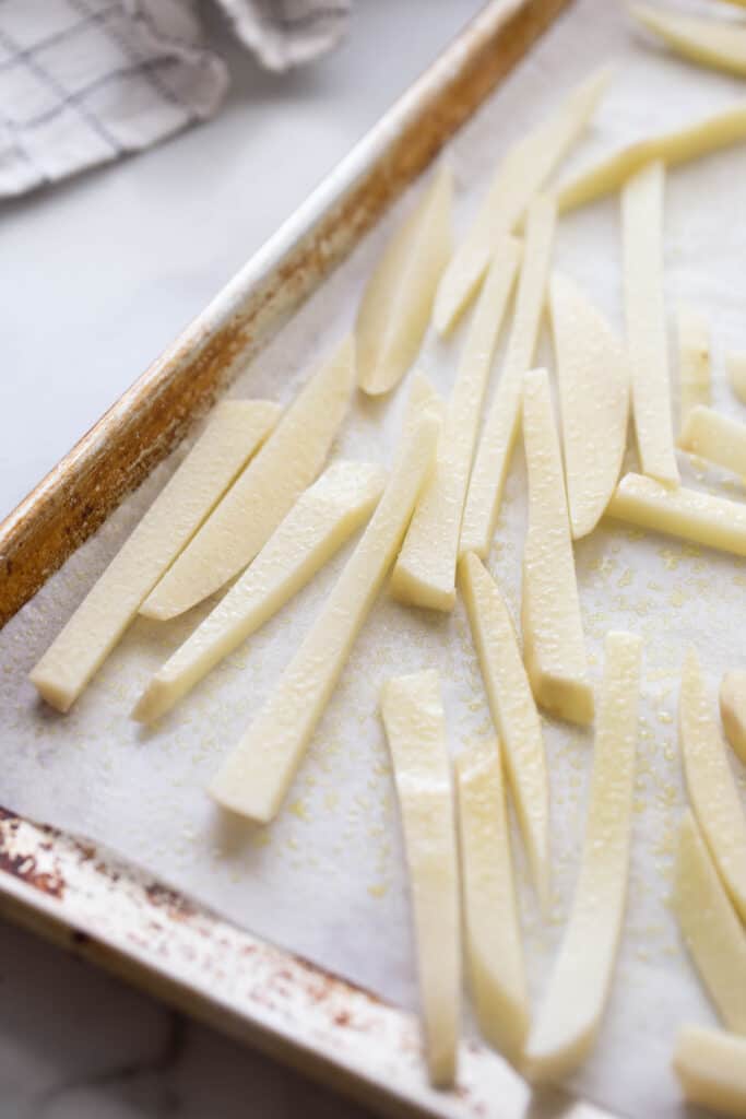 A baking sheet with hand cut french fries on parchment paper.