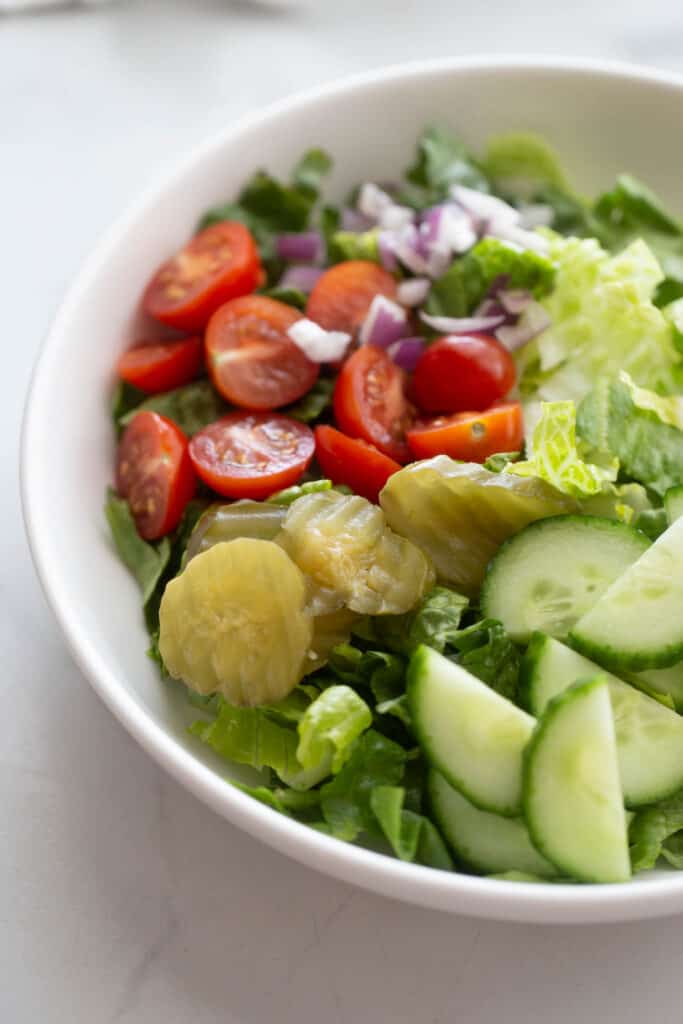 A bowl of romaine lettuce, pickles, cucumbers, tomatoes, and red onions.