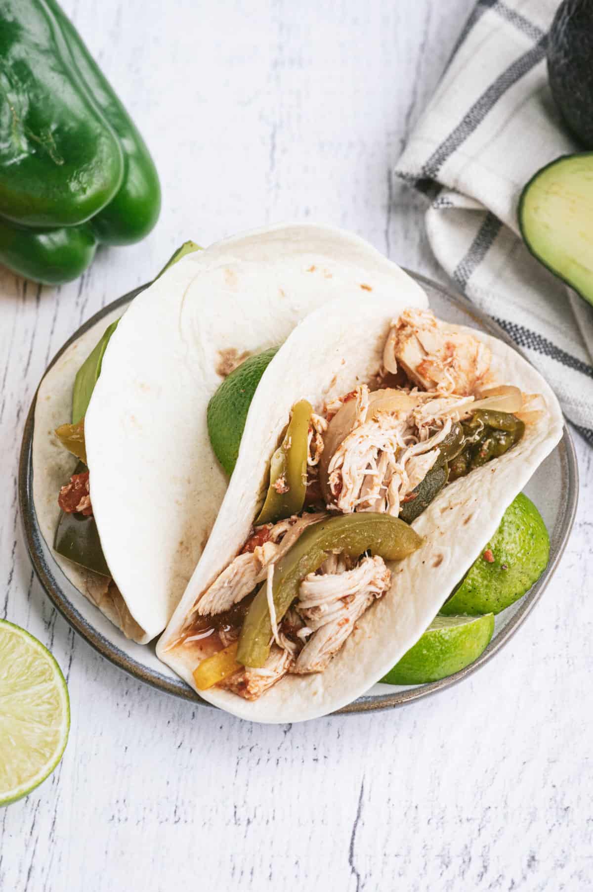 White corn tortillas with crockpot chicken fajitas inside on a plate with sliced lime.