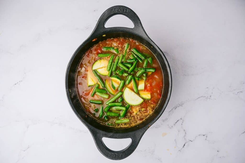 A cast iron pot of Chicken Vegetable Soup topped with fresh green beans and zucchini.
