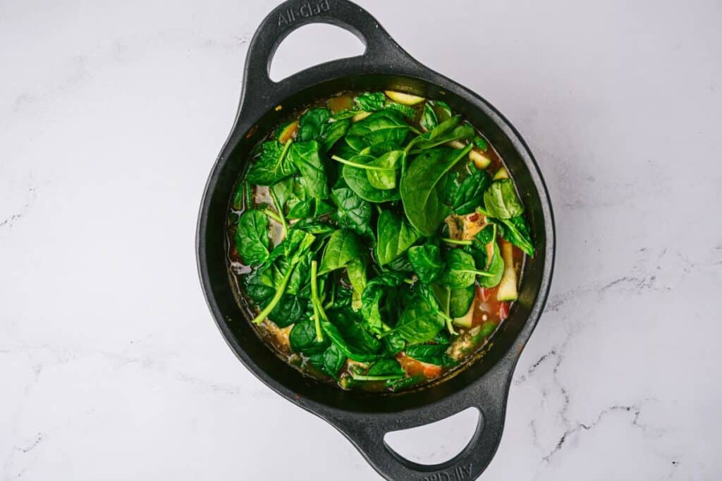 Cast iron pot with Chicken Vegetable Soup layered with fresh spinach.
