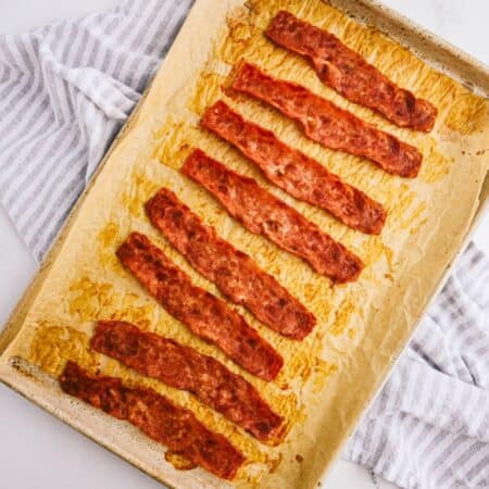 A baking pan covered with parchment paper and crispy oven baked turkey bacon on a kitchen towel.