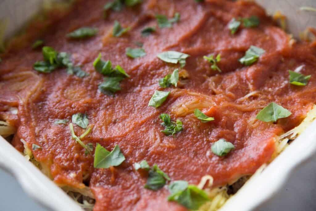 Spaghetti squash topped with sauce and basil in a baking dish.