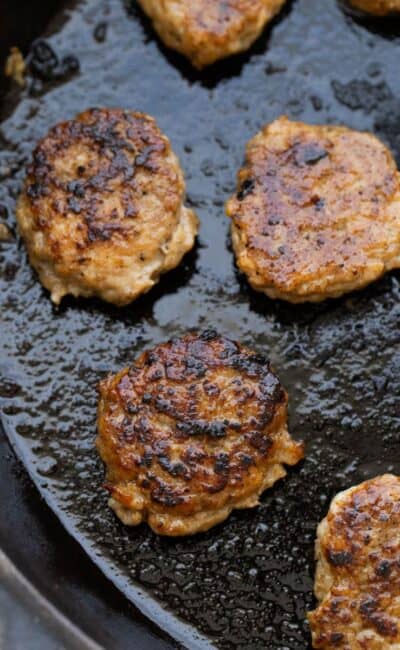 A cast iron skillet with homemade chicken sausage patties cooked golden brown.