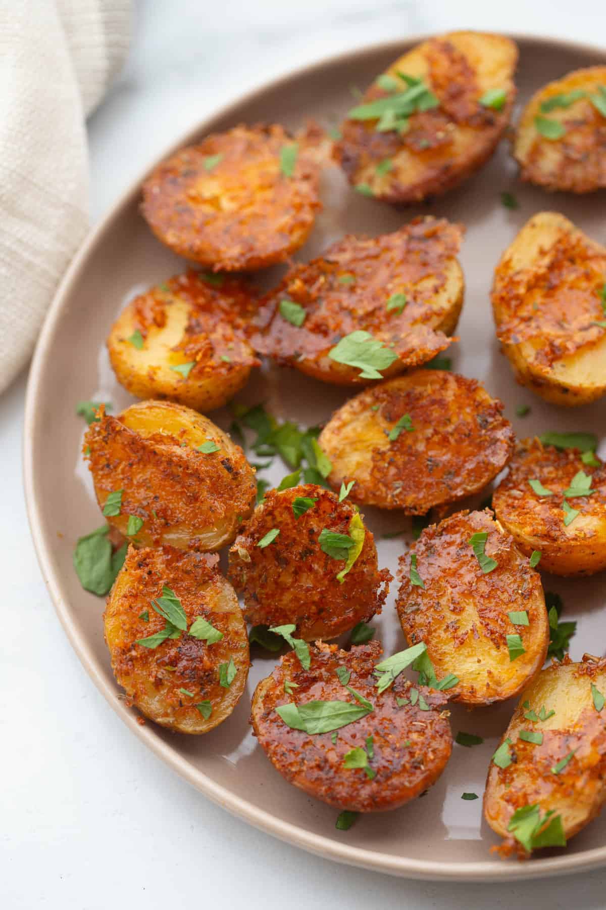 Crispy oven roasted baby potatoes on a round rimmed plate with parmesan cheese and fresh parsley as garnish.