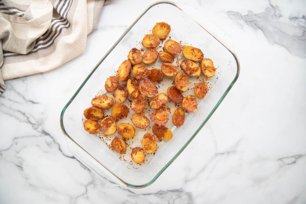 Glass pan with crispy parmesan roasted baby potatoes on a white marble counter.
