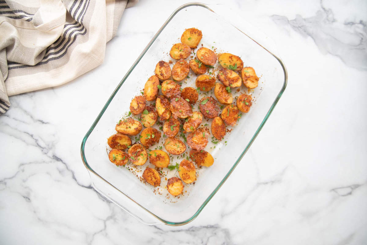 Glass pan with crispy parmesan roasted baby potatoes on a white marble counter.