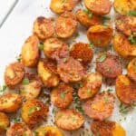 Crispy oven roasted baby potatoes in a glass pan with parmesan cheese and fresh parsley as garnish.