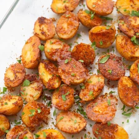 Crispy oven roasted baby potatoes in a glass pan with parmesan cheese and fresh parsley as garnish.