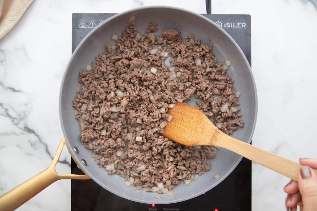 Ground beef and onions being cooked in a skillet.