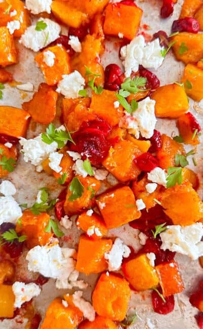 Sheet pan with roasted butternut squash and cranberries topped with goat cheese and fresh parsley.