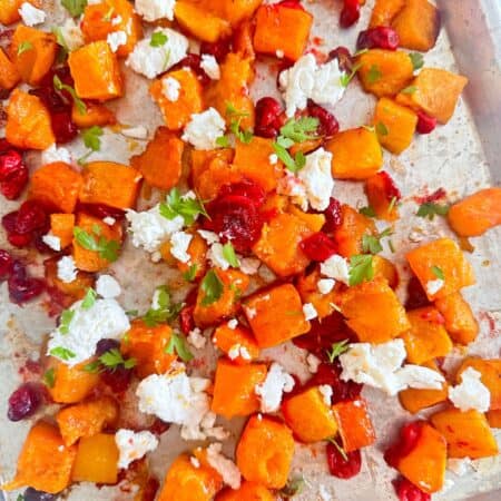 Sheet pan with roasted butternut squash and cranberries topped with goat cheese and fresh parsley.