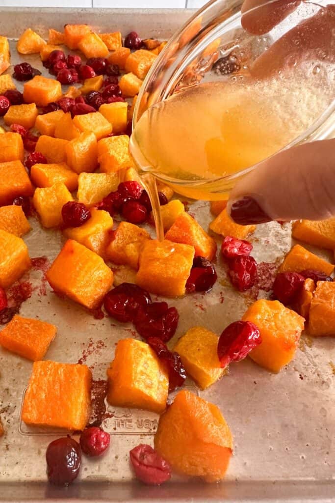 Honey being drizzled over oven roasted butternut squash and cranberries on a sheet pan.