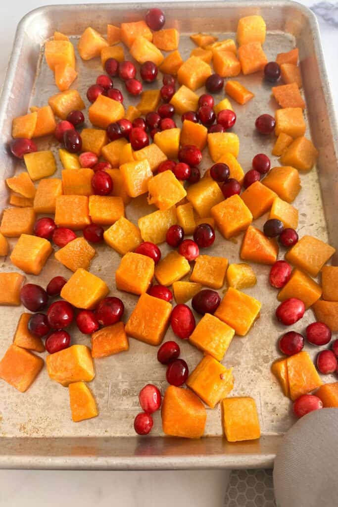 Photo of a sheet pan with butternut squash cubes and cranberries.