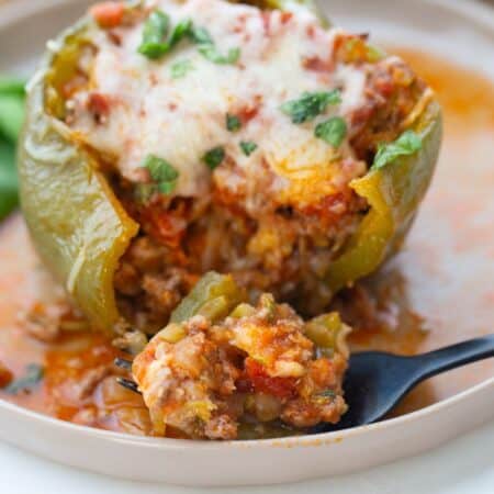 An Italian Stuffed Green Bell Pepper topped with cheese with a fork full of a bite of filling on a white rimmed plate.