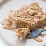 A piece of coffee cake baked oatmeal on a rimmed plate drizzled with peanut butter.
