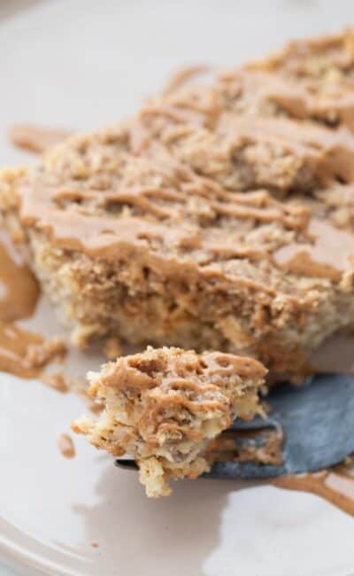 A piece of coffee cake baked oatmeal on a rimmed plate drizzled with peanut butter.