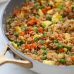 A skillet with brown hibachi fried rice with veggies, peas, and eggs.