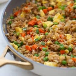 A skillet with brown hibachi fried rice with veggies, peas, and eggs.