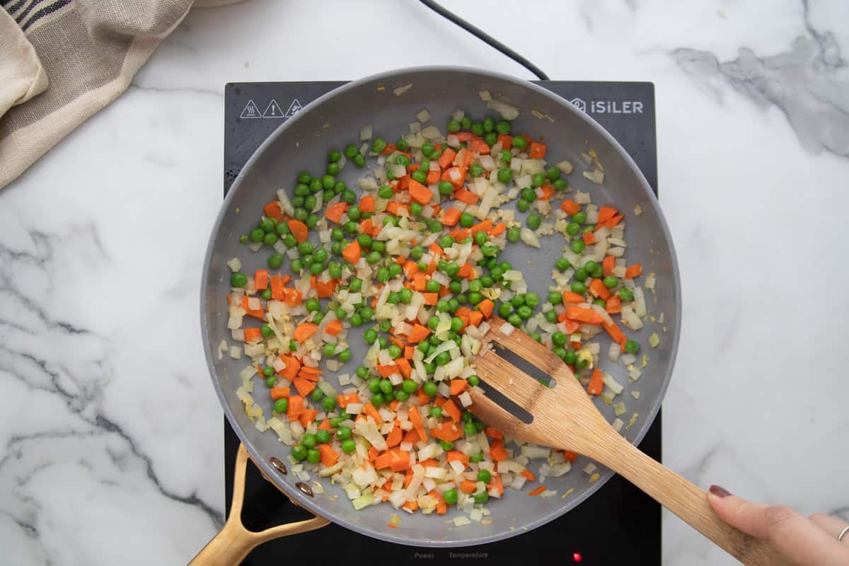 Fresh veggies and frozen peas in a skillet for fried rice.