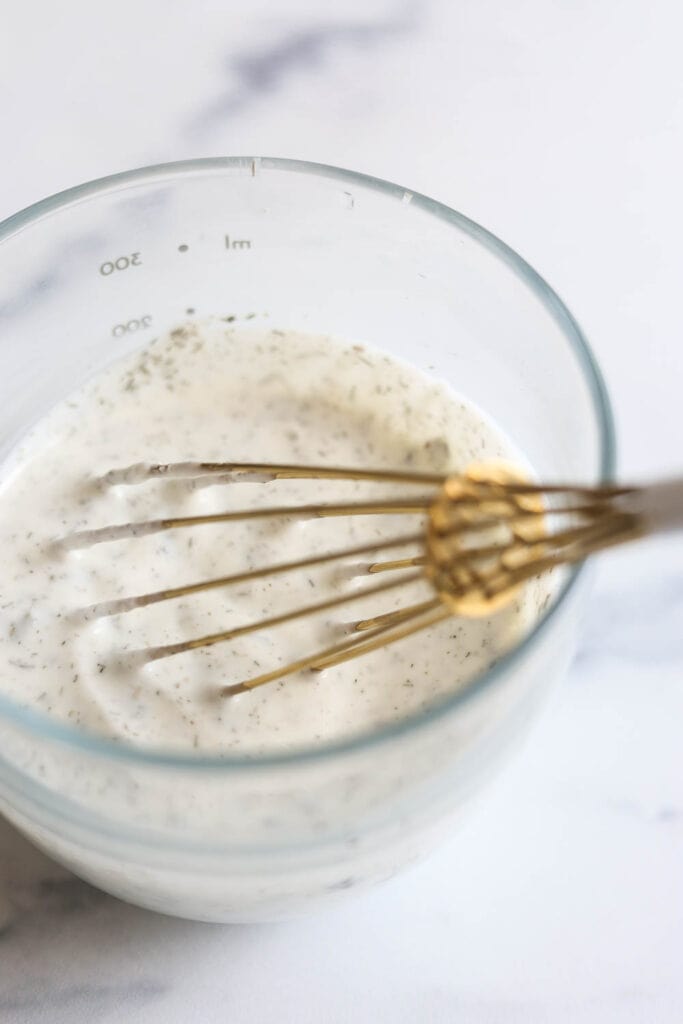 Homemade Greek Yogurt ranch dressing in a small glass jar with a small gold whisk inside.