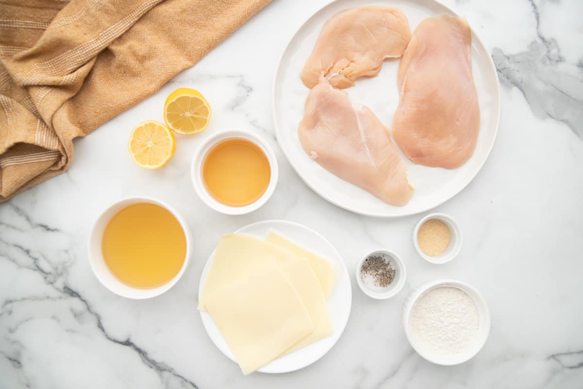 Ingredients for chicken scallopini on a white marble table.
