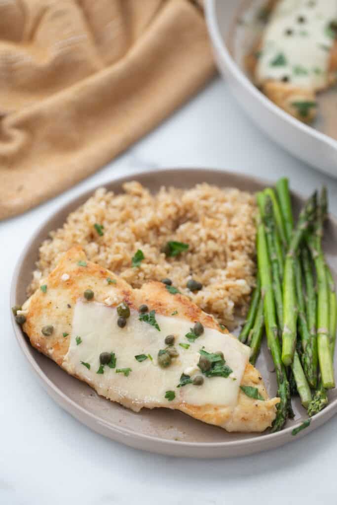 Plated dinner with thinly sliced chicken in a lemon butter sauce with brown rice and roasted asparagus.