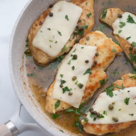 Chicken scallopini in a white ceramic pan topped with thin mozzarella, capers, and fresh parsley.